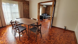 A dining area with a wooden table and chairs, a brick wall, and a view into a living room with a sofa and a table. - Yarra Valley Motel (Lilydale)