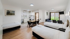 A modern, well-lit room with a kitchenette, a dining area, and a seating area with a sofa and chairs. - Yarra Valley Motel (Lilydale)
