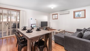 A modern living room with a dining area, a grey sofa, and a flat-screen TV. - Yarra Valley Motel (Lilydale)