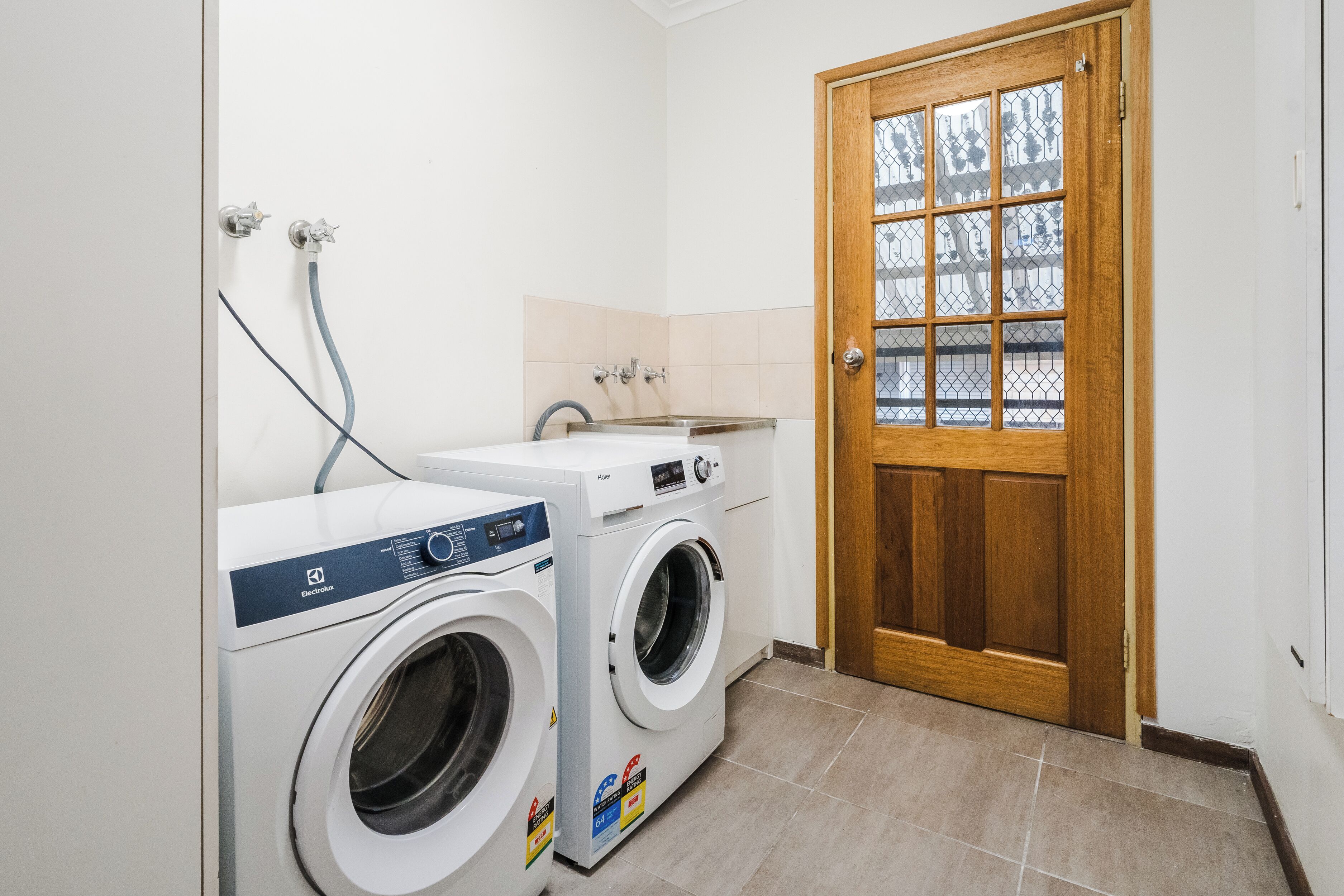 A laundry room with two front-loading washing machines, a sink, and a wooden door with a glass panel.