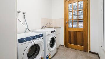 A laundry room with two front-loading washing machines, a sink, and a wooden door with a glass panel.