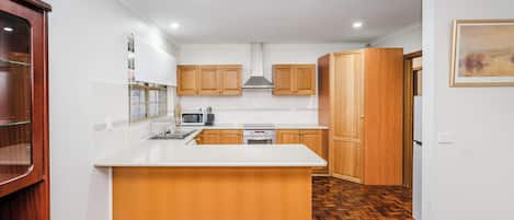 A modern kitchen with wooden cabinets, a central island, and a herringbone-patterned floor.