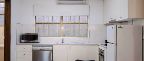 A compact kitchen with white cabinets, a microwave, a refrigerator, and a dishwasher.