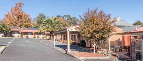 A motel with a parking lot, covered outdoor seating, and a row of rooms with brick facades.