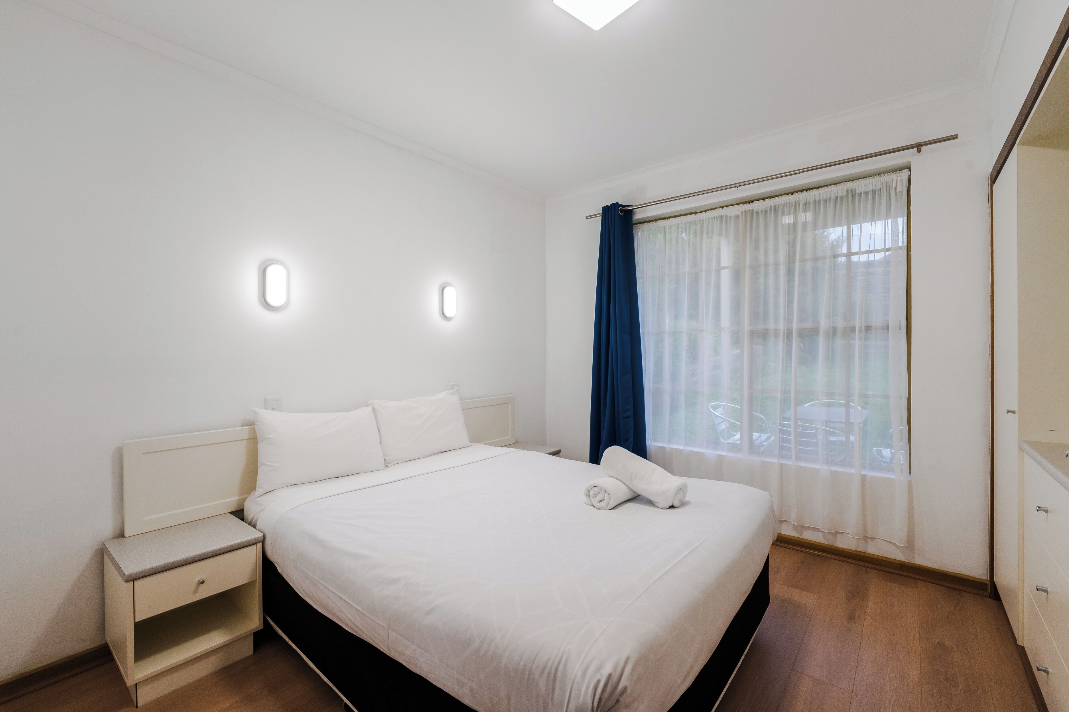 Een slaapkamer met een bed, nachtkastjes, een raam met gordijnen en een plafondlamp.