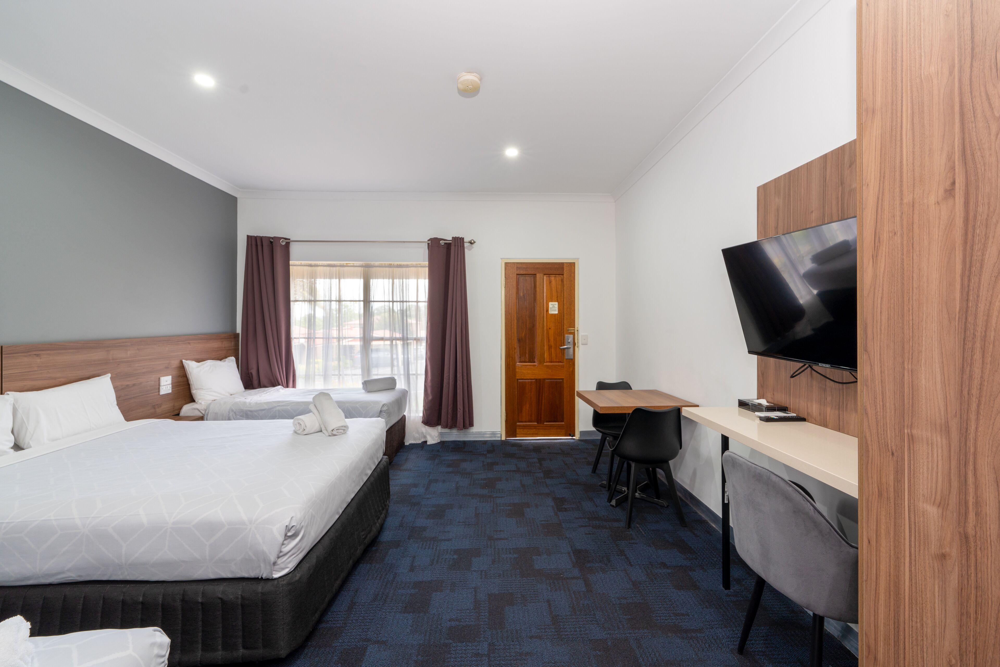 A hotel room with two beds, a desk, a chair, a television, and a door.