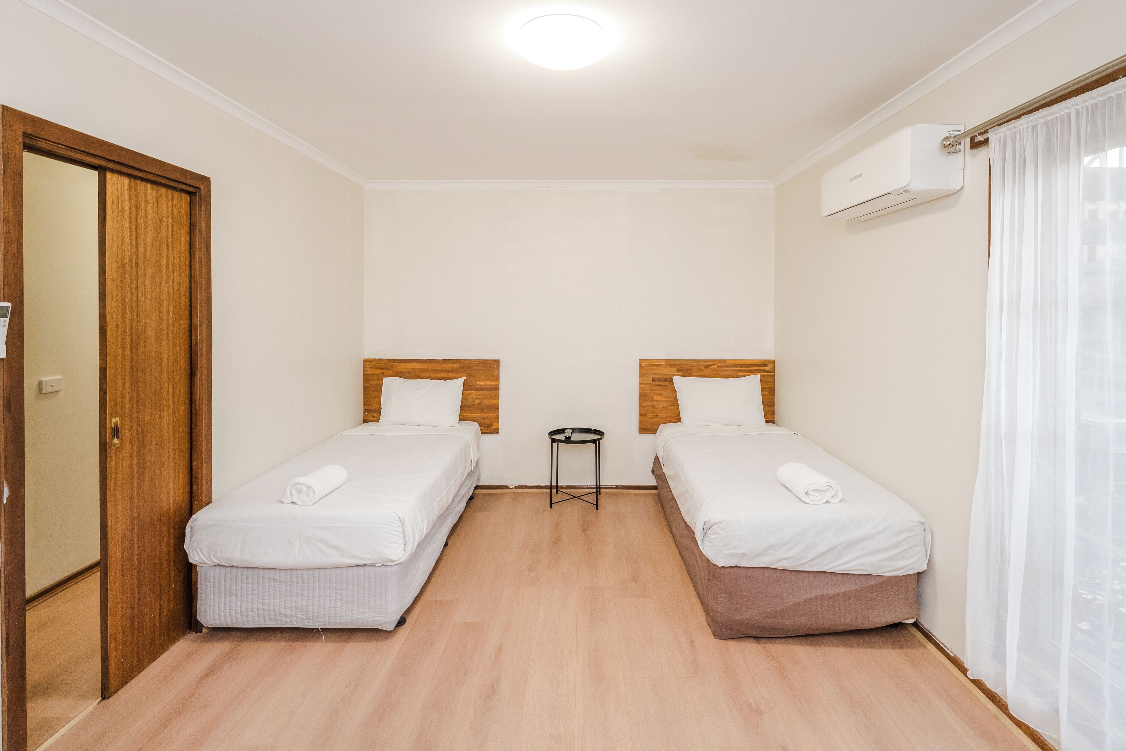 A small, clean room with two single beds, a small table, and a door.