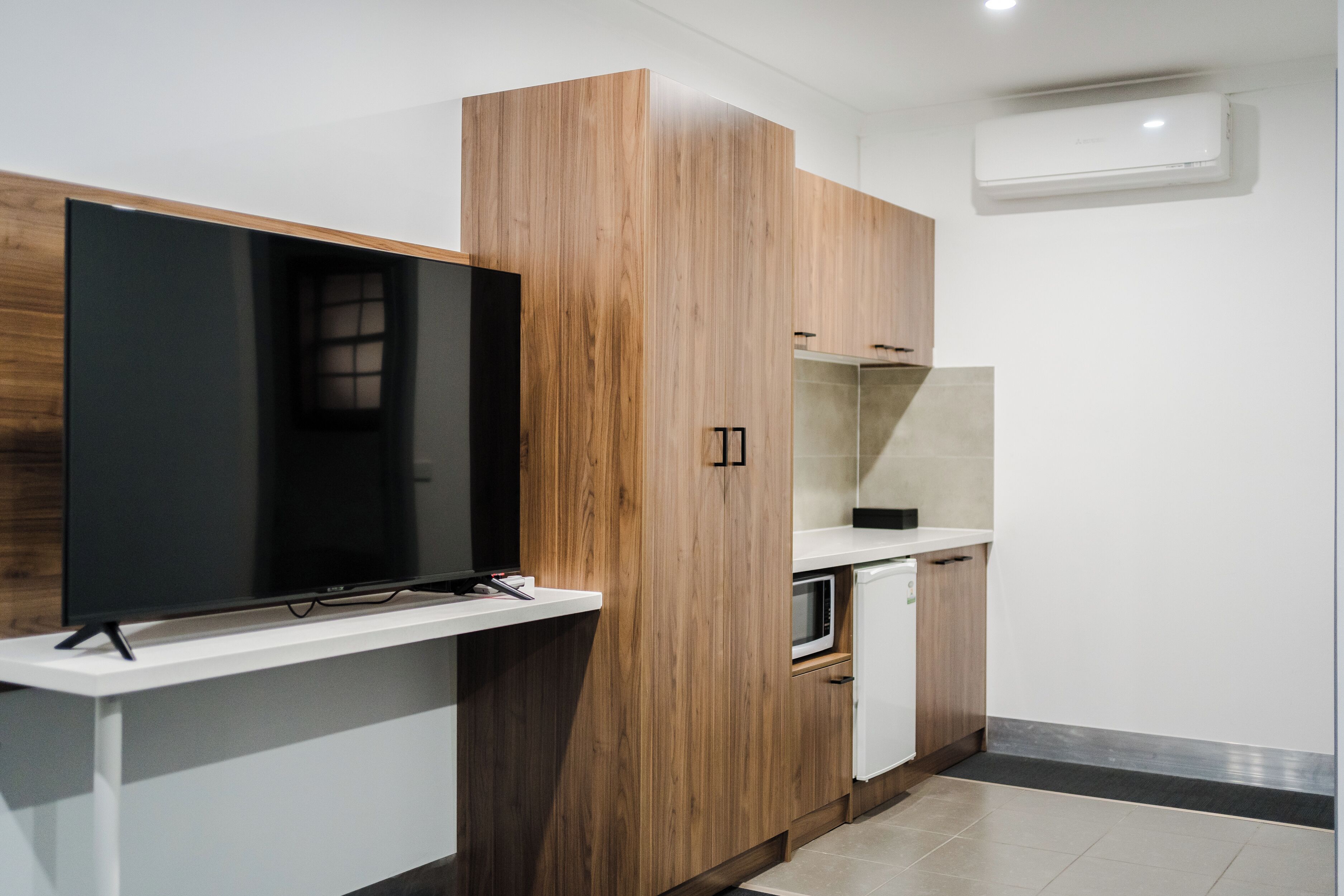 Cocina moderna con televisión integrada, armarios de madera, microondas y refrigerador pequeño.