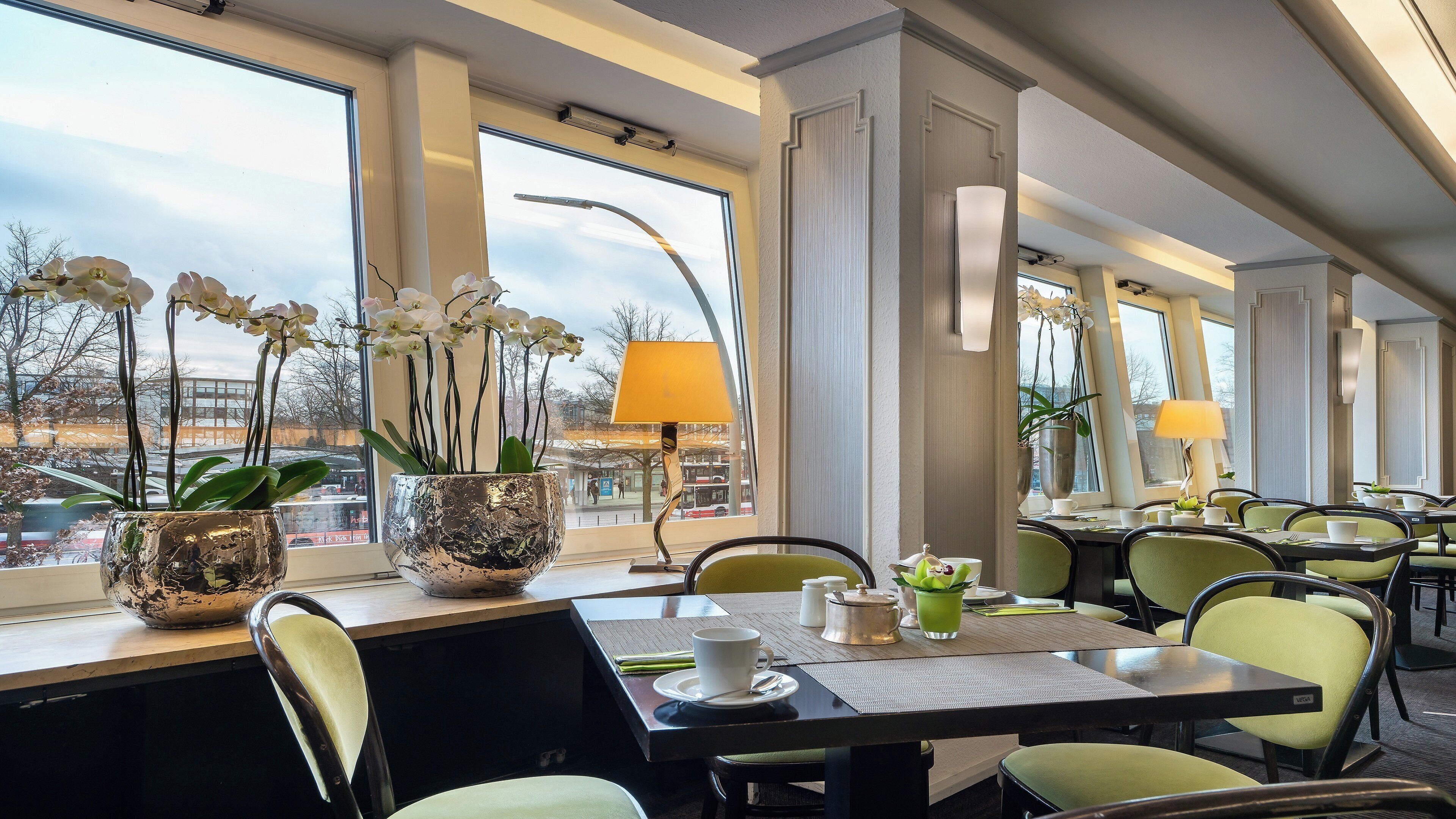 A restaurant with tables, chairs, potted orchids, and a view of the city.
