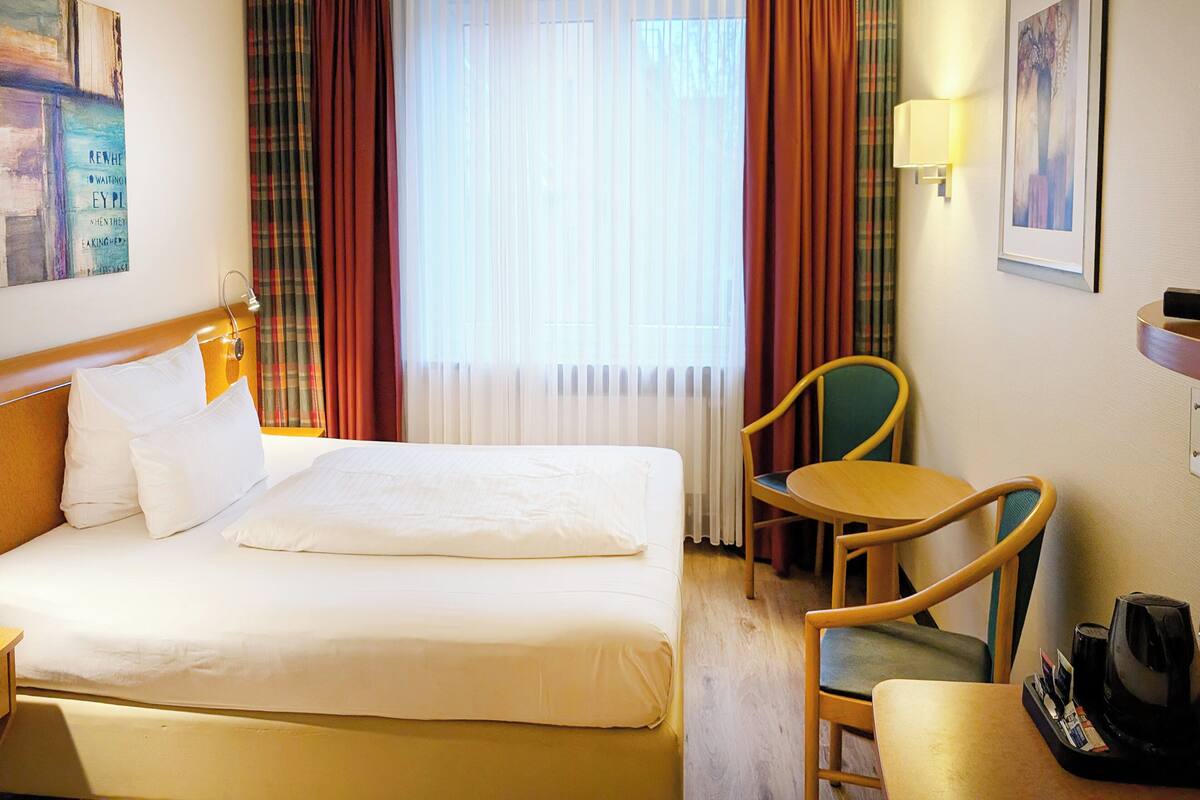 A hotel room with a bed, a chair, a table, and a coffee maker.