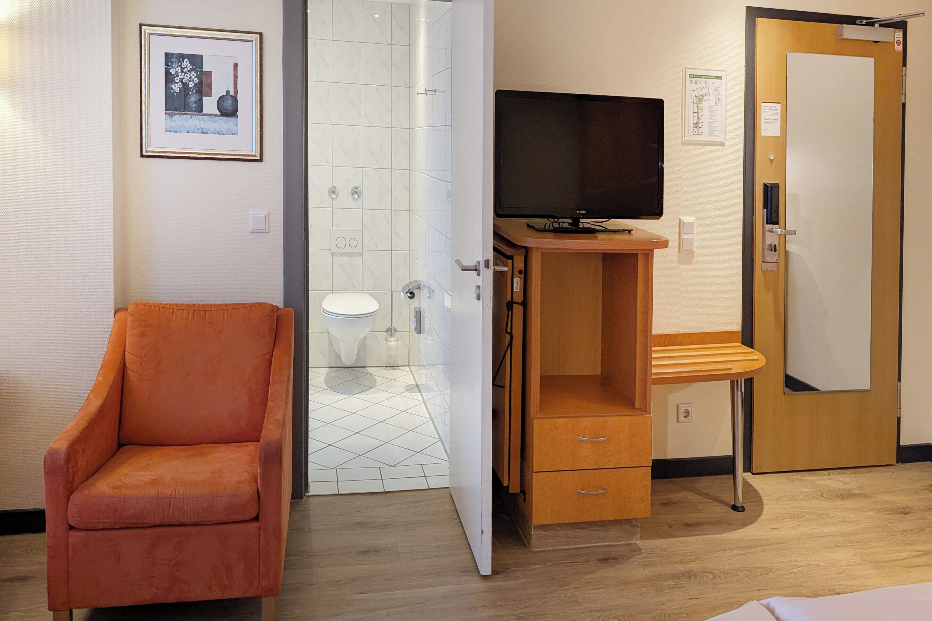 Una habitación de hotel con un armario de madera, un televisor, una puerta y una silla.