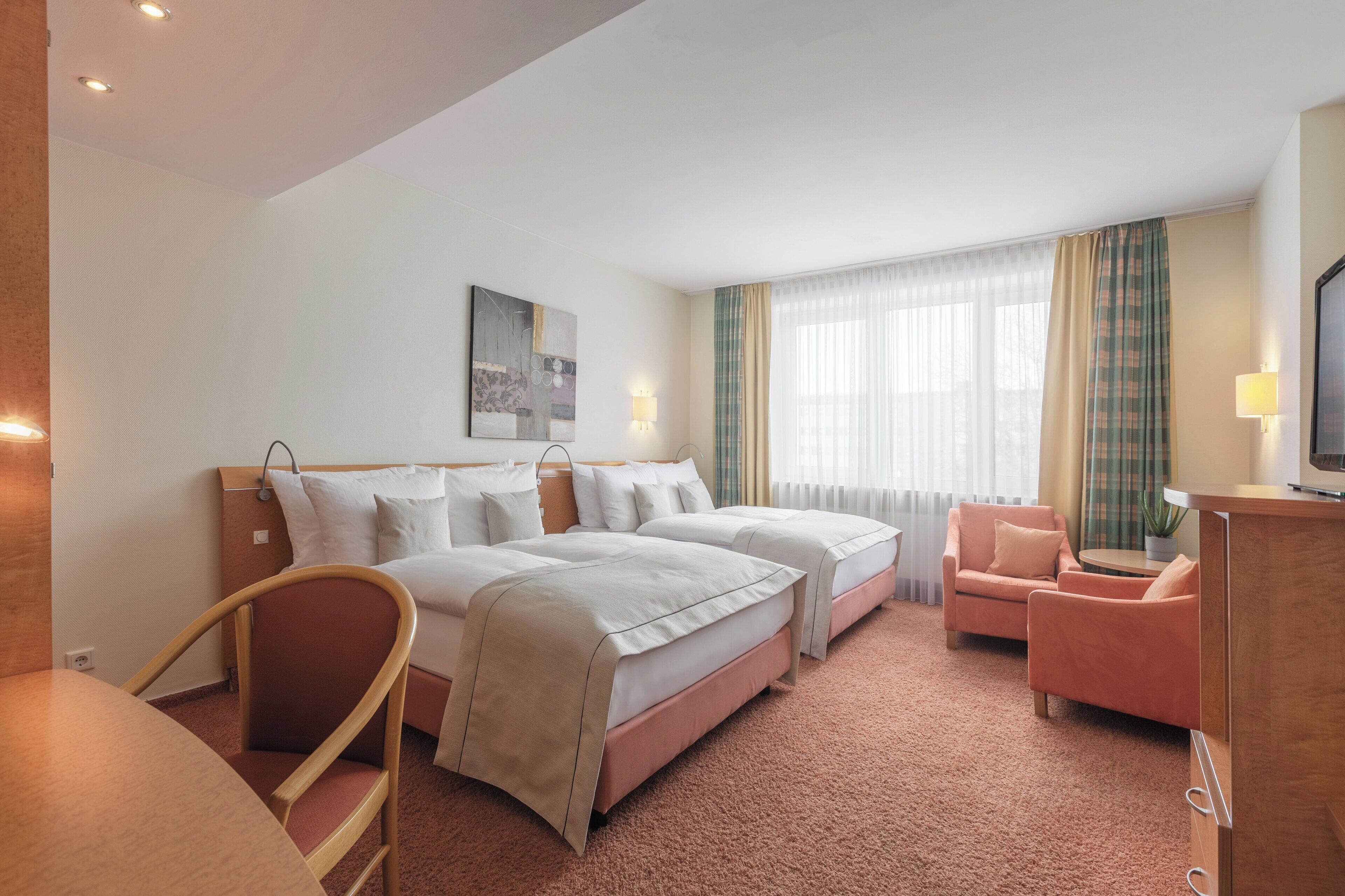 Habitación de hotel con dos camas, un escritorio, una silla, un televisor y una ventana con cortinas.