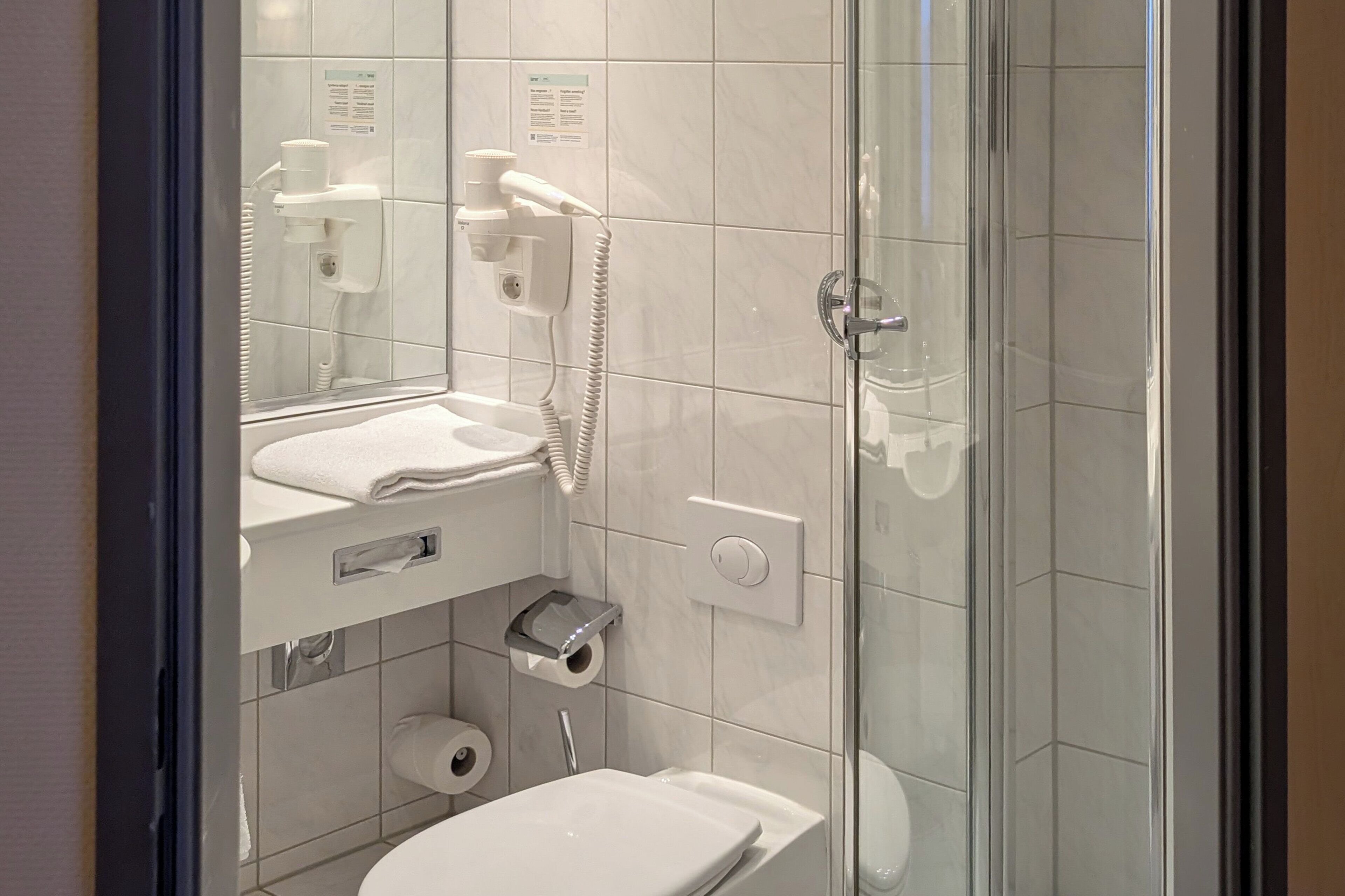 A modern bathroom with a glass-enclosed shower, a toilet, and a hairdryer mounted on the wall.