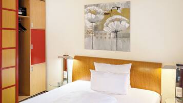 A hotel room with a bed, a wooden headboard, a wardrobe, and a wall-mounted painting.