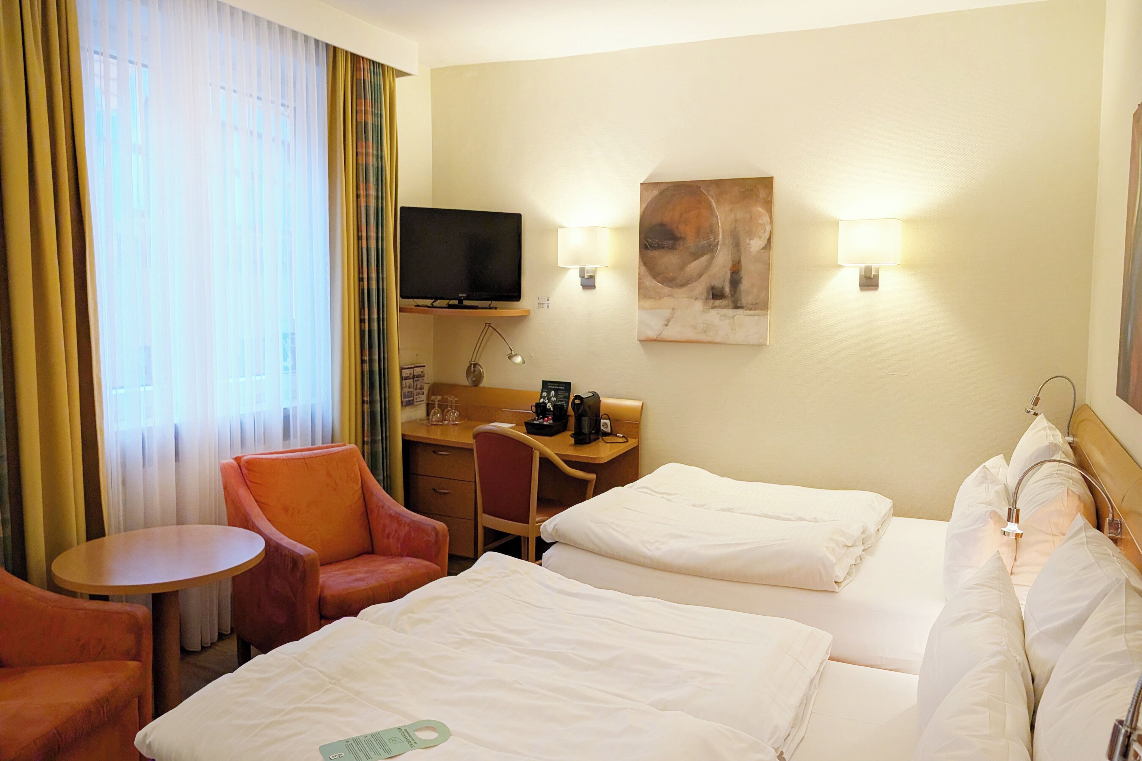 A hotel room with two beds, a desk, a chair, a television, and a painting on the wall.