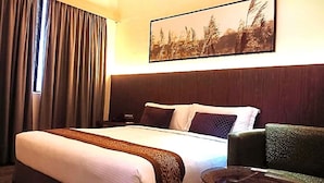 A hotel room with a large bed, a headboard, a nightstand, a chair, and a painting on the wall. - GoodHope Hotel Skudai (Johor Bahru)