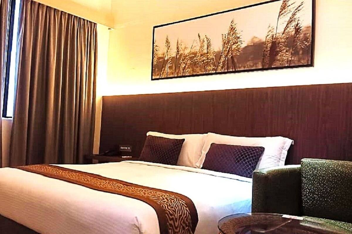Une chambre d’hôtel avec un grand lit, une tête de lit, une table de chevet, une chaise et un tableau au mur.