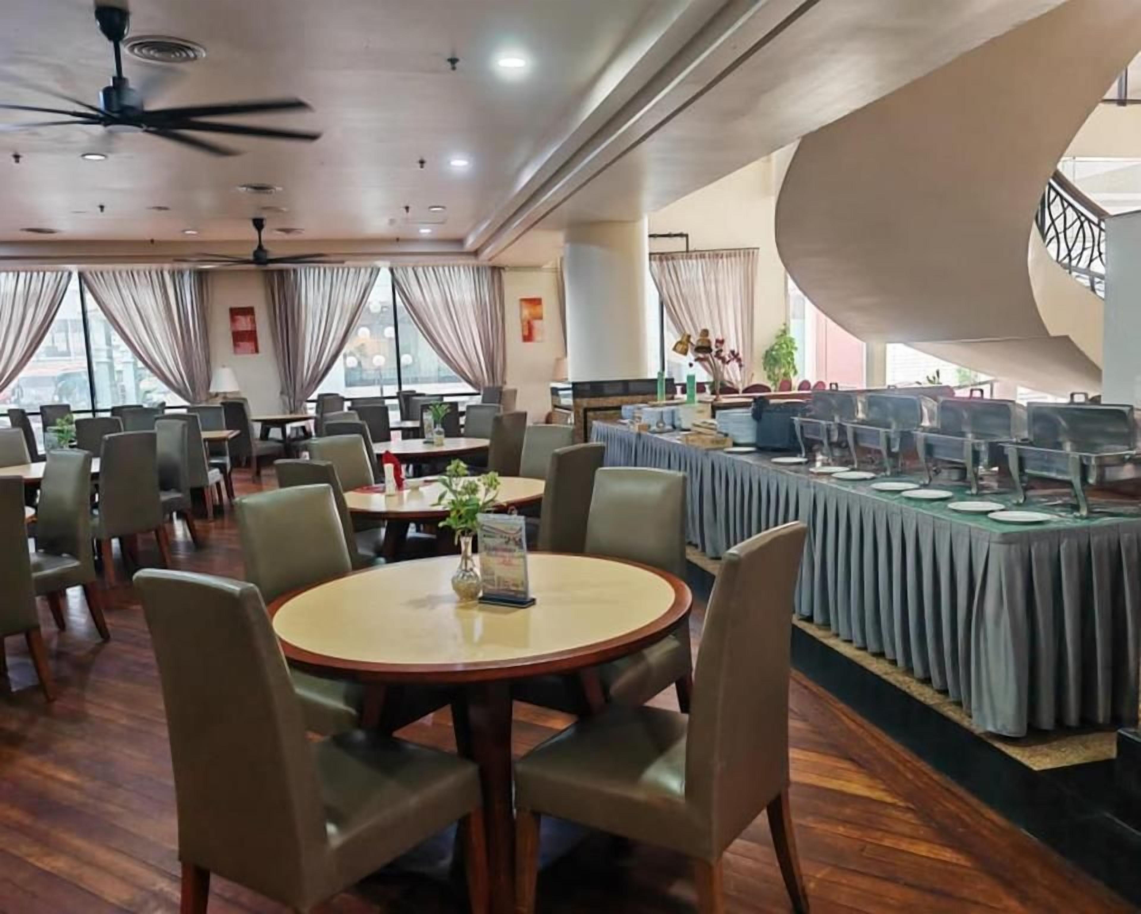 Un'area ristorazione in hotel con tavoli rotondi, sedie e un'area buffet.
