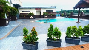 Uma área de piscina no terraço com deck de madeira, plantas em vasos e um edifício ao fundo.