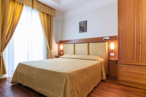 Una habitación de hotel con cama, cortinas, un cuadro en la pared y un armario de madera.