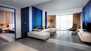 Una habitación de hotel moderna con un sofá grande, una mesa de centro, un televisor y un escritorio.