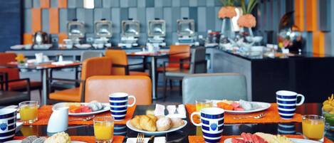 A breakfast buffet with various food items and orange chairs in a modern dining area.