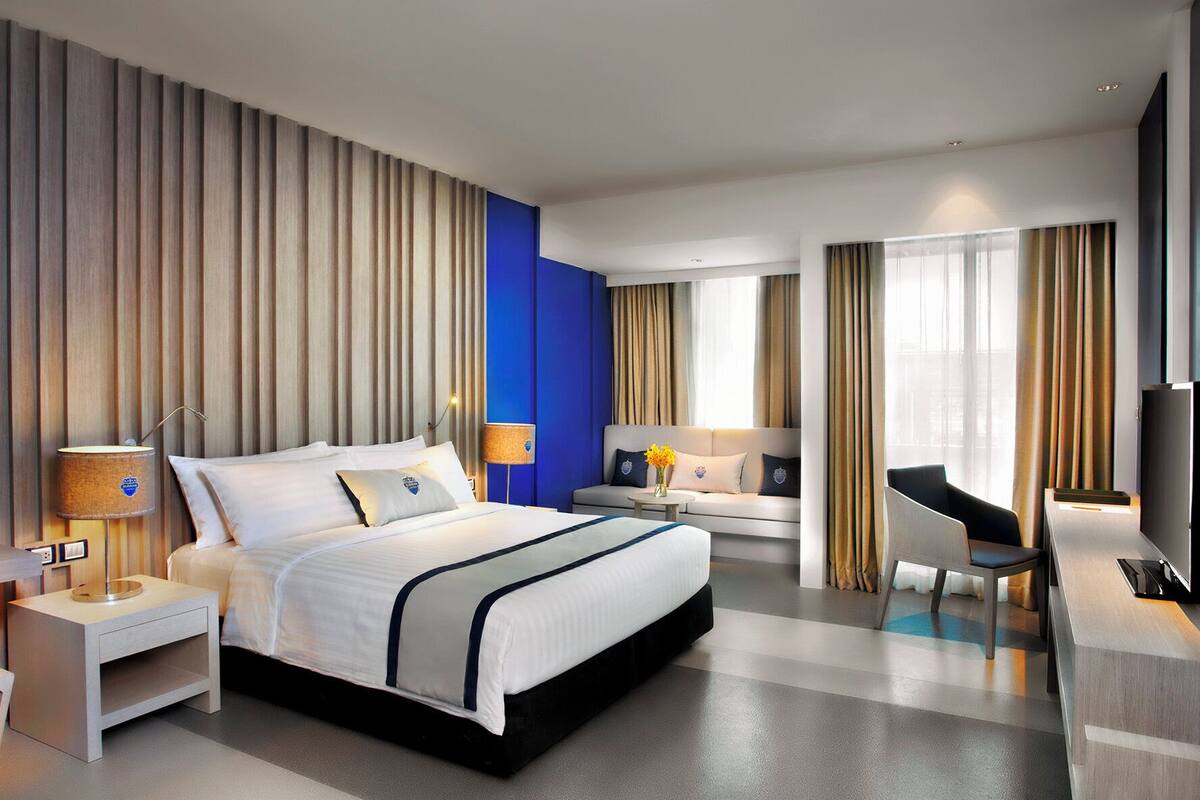 A modern hotel room with a large bed, bedside tables, a desk, a chair, and a TV.