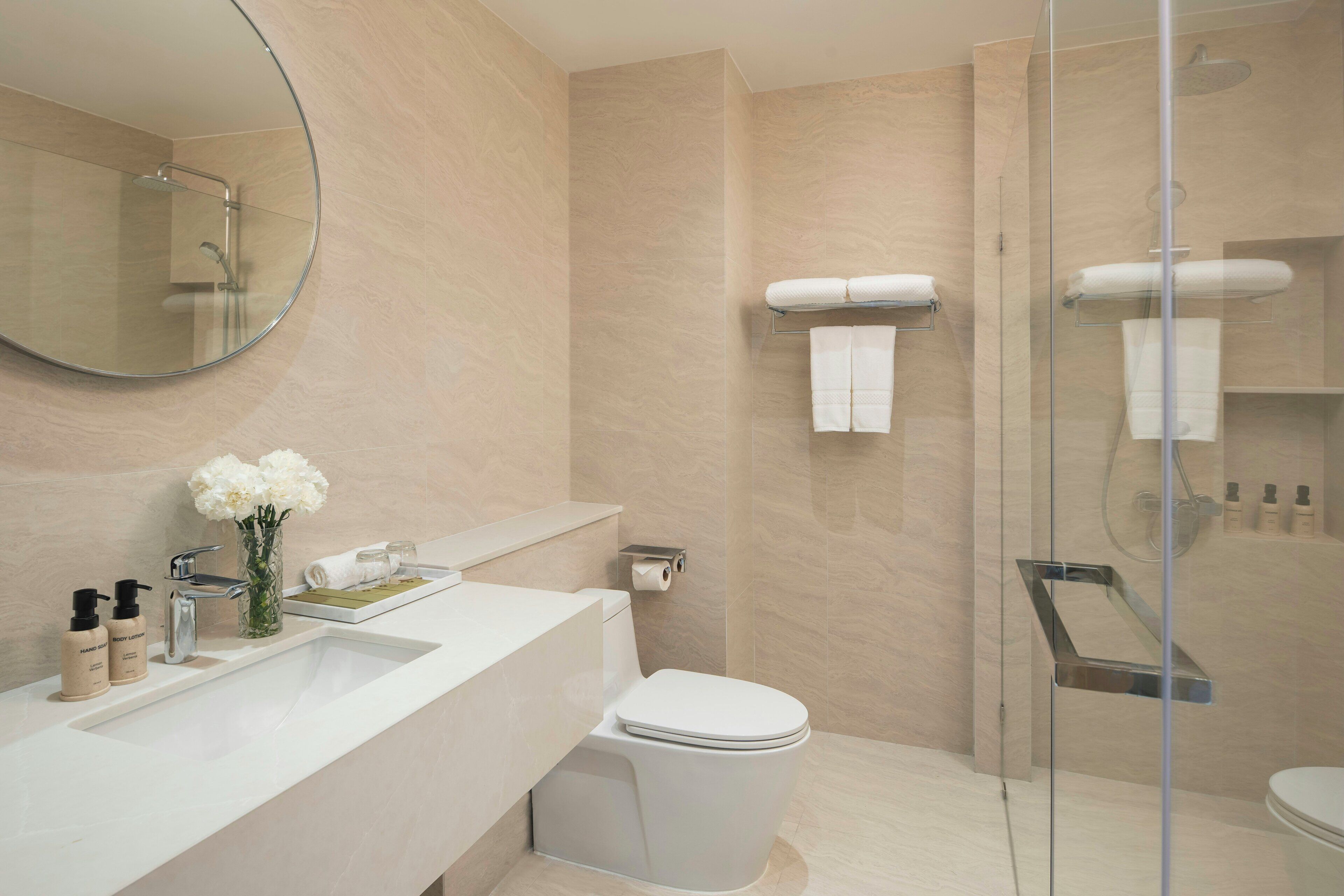 Une salle de bain moderne avec un grand miroir rond, un lavabo blanc, des toilettes et une douche à parois de verre.