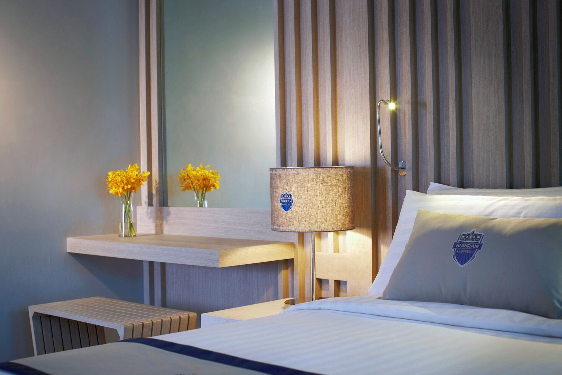 A hotel room with a bed, a bedside table with a lamp, and a mirror.