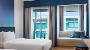 Habitación de hotel con dos camas, un sofá, una mesita y ventana con cortinas, y vista a un edificio.