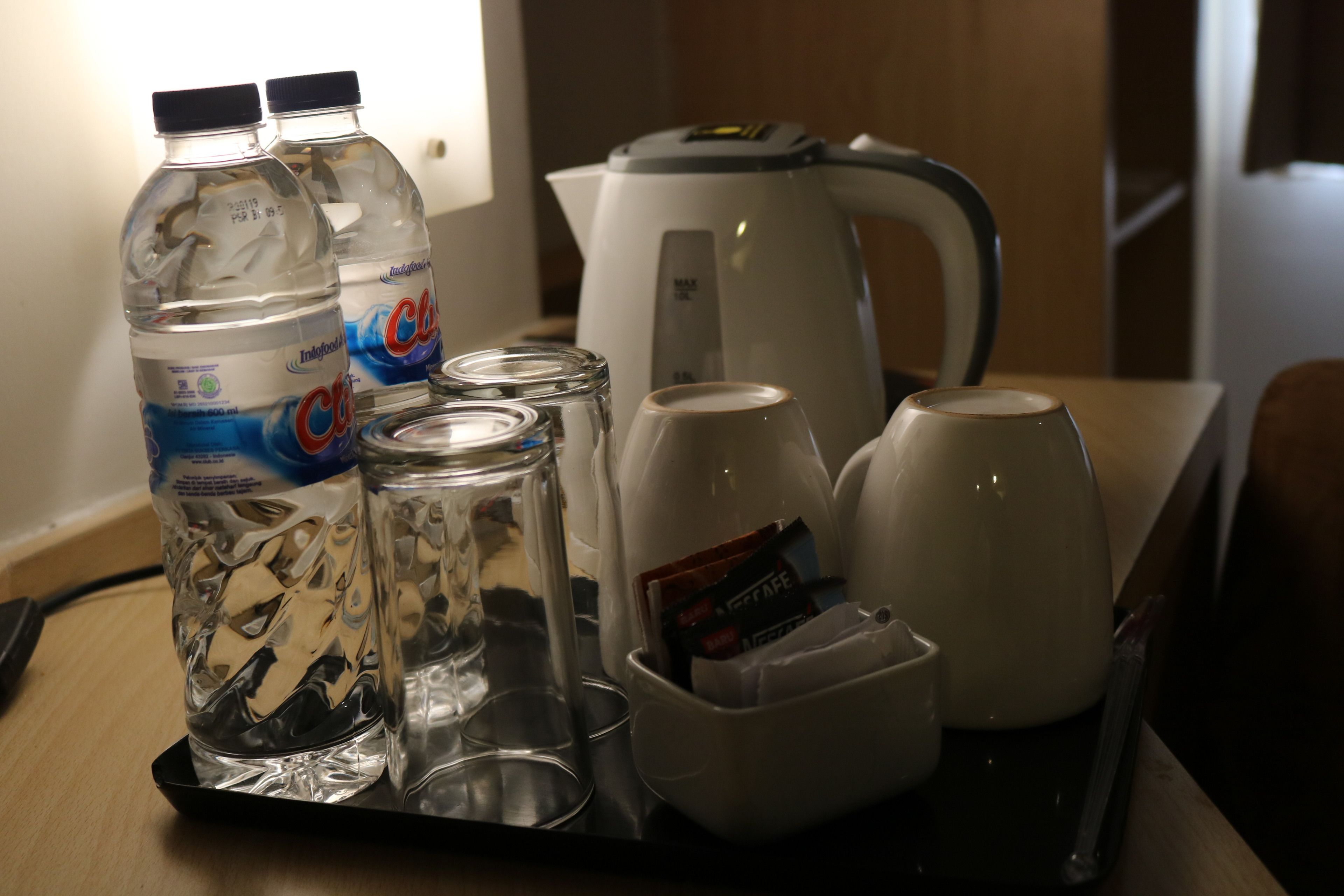 A tray with two bottles of water, two glasses, two cups, and a coffee maker.
