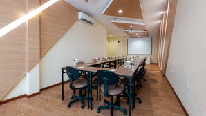 Ein Konferenzraum mit langen Tischen, Stühlen, einer Projektionsleinwand und einer Uhr an der Wand.