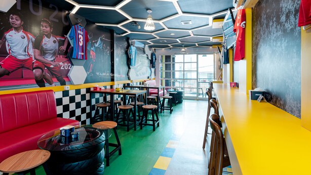 Ein lebhaftes Restaurant mit auffälligem, sechseckigem Deckenstil, roten Sitzmöglichkeiten und einem Wandgemälde zum Thema Sport.