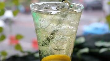 A tall glass with a straw, filled with a beverage and ice cubes, garnished with a slice of lemon, on a dark cloth.