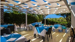 An outdoor covered patio area with tables set up for dining, surrounded by greenery and a clear view of the sky. - Village Camping La Foce (Valledoria)