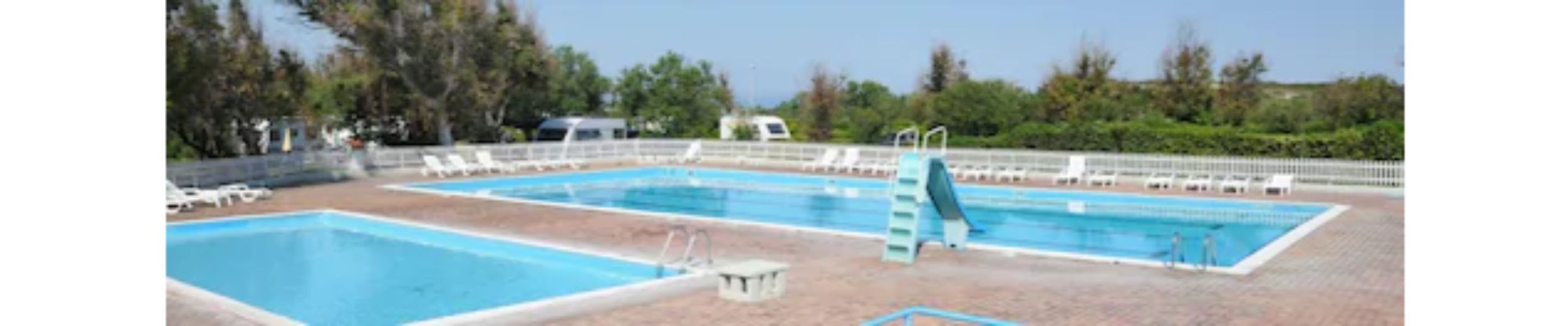 Una piscina con dos carriles, rodeada de sillas de descanso y un puesto de socorrista.