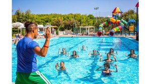 A swimming pool with people in the water, surrounded by a water park with slides and play structures. - Village Camping La Foce (Valledoria)