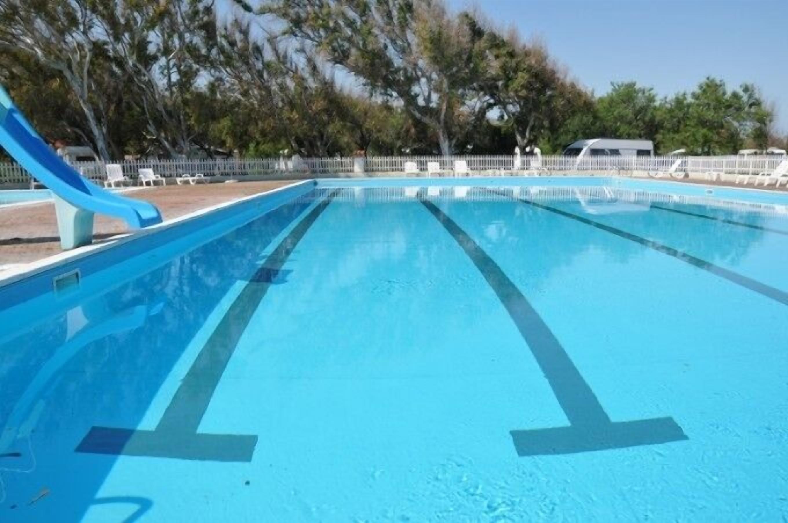 Ein klares Schwimmbecken mit Bahnen, umgeben von einem Zaun und Bäumen.