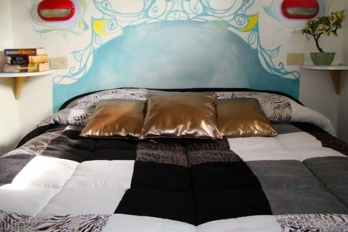 A bed with a checkered bedspread, three pillows, and a decorative headboard with wall art.