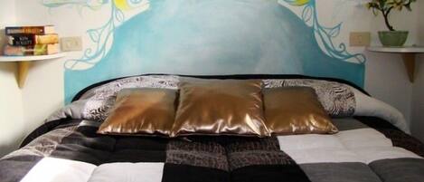A bed with a checkered bedspread, three pillows, and a decorative headboard with wall art.