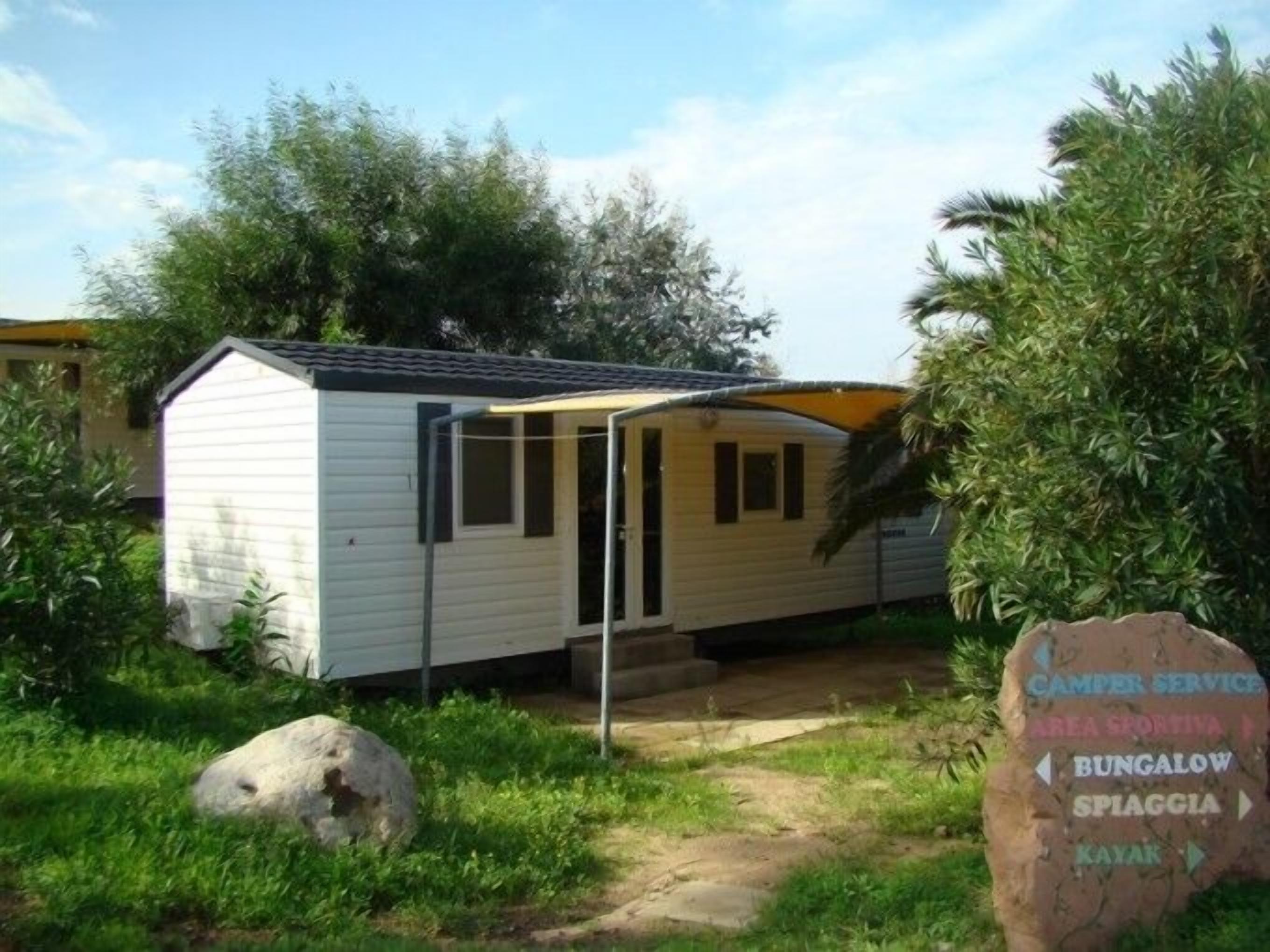 A small, single-story mobile home with a porch and a covered outdoor area.