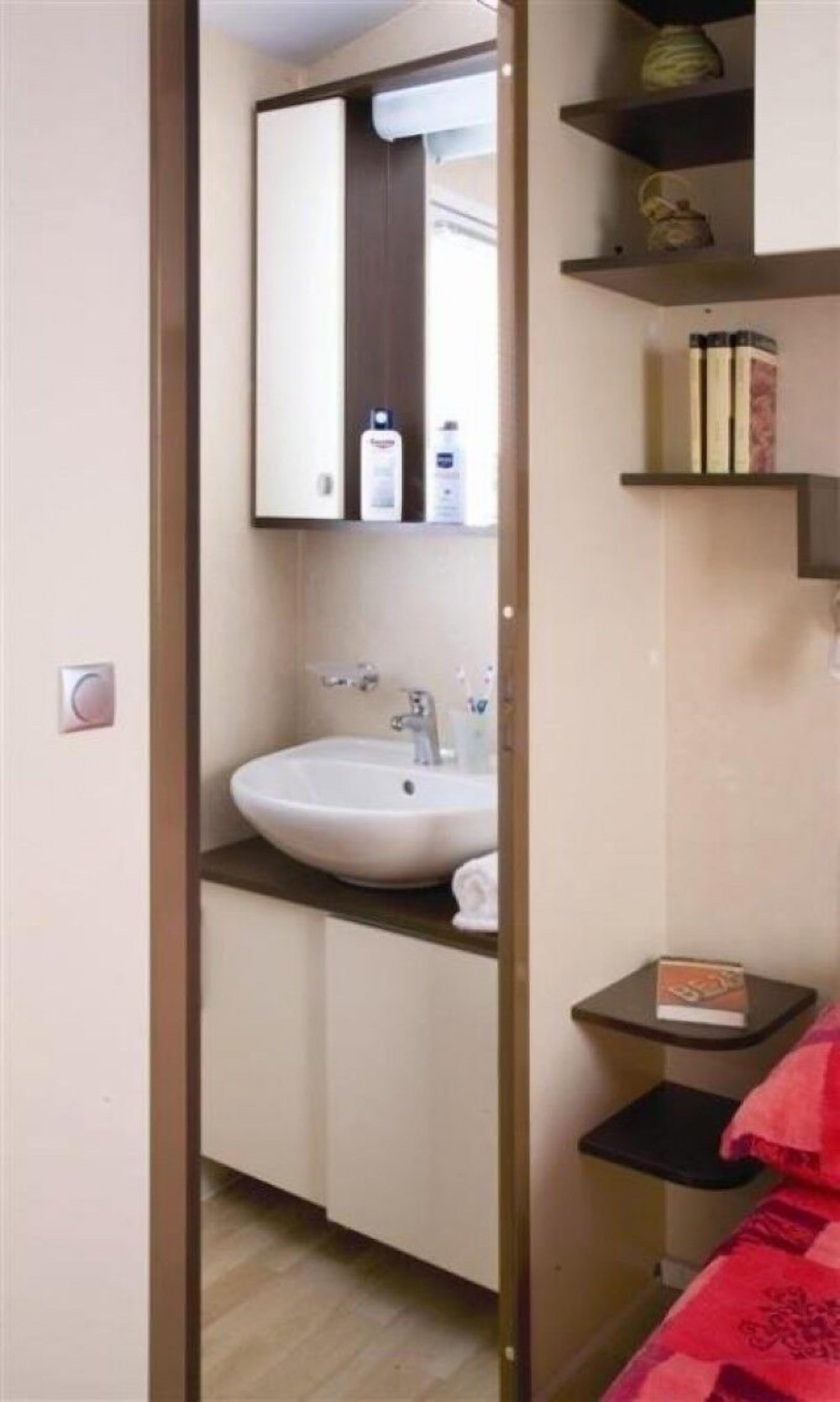 Een badkamer met een wastafel, spiegel en planken met toiletartikelen.
