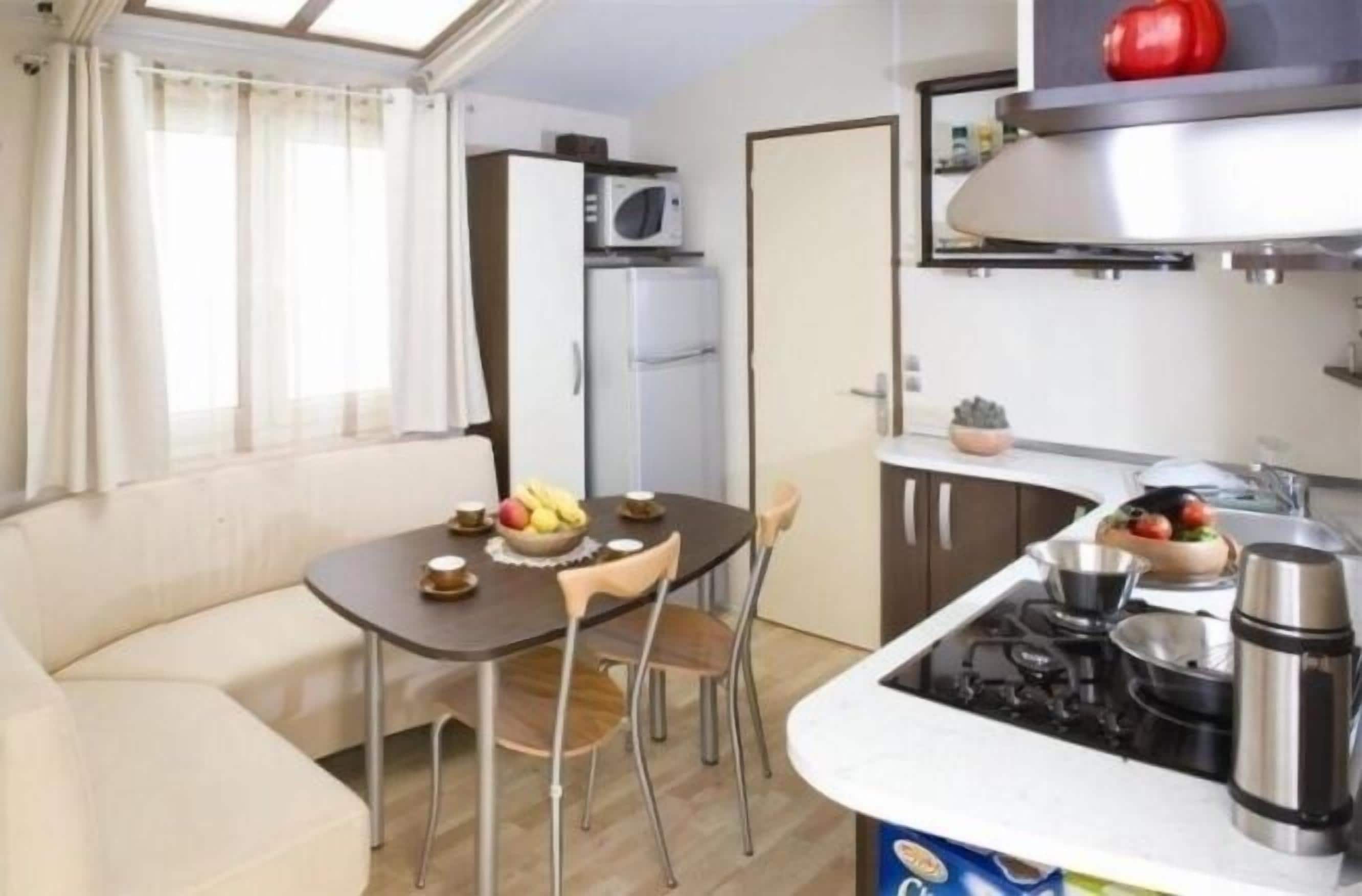 Een functionele keuken met een eettafel, stoelen, een koelkast, een magnetron en een fornuis.