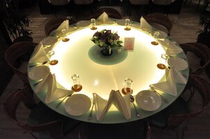 Una mesa redonda de comedor con un arreglo floral central, rodeada de sillas y puesta con platos, vasos y cubiertos.