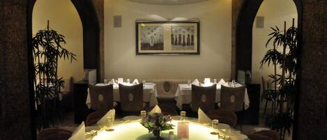 A formal dining room with a round table, chairs, and a central floral arrangement.