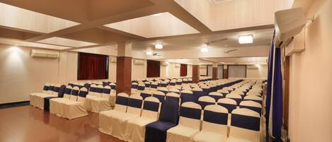 A large hall with rows of chairs and tables, air conditioning units, and a ceiling with recessed lighting.