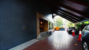 A covered walkway leading to a building with a dark exterior wall and a wooden entrance. - Abbott Hotel (Navi Mumbai)