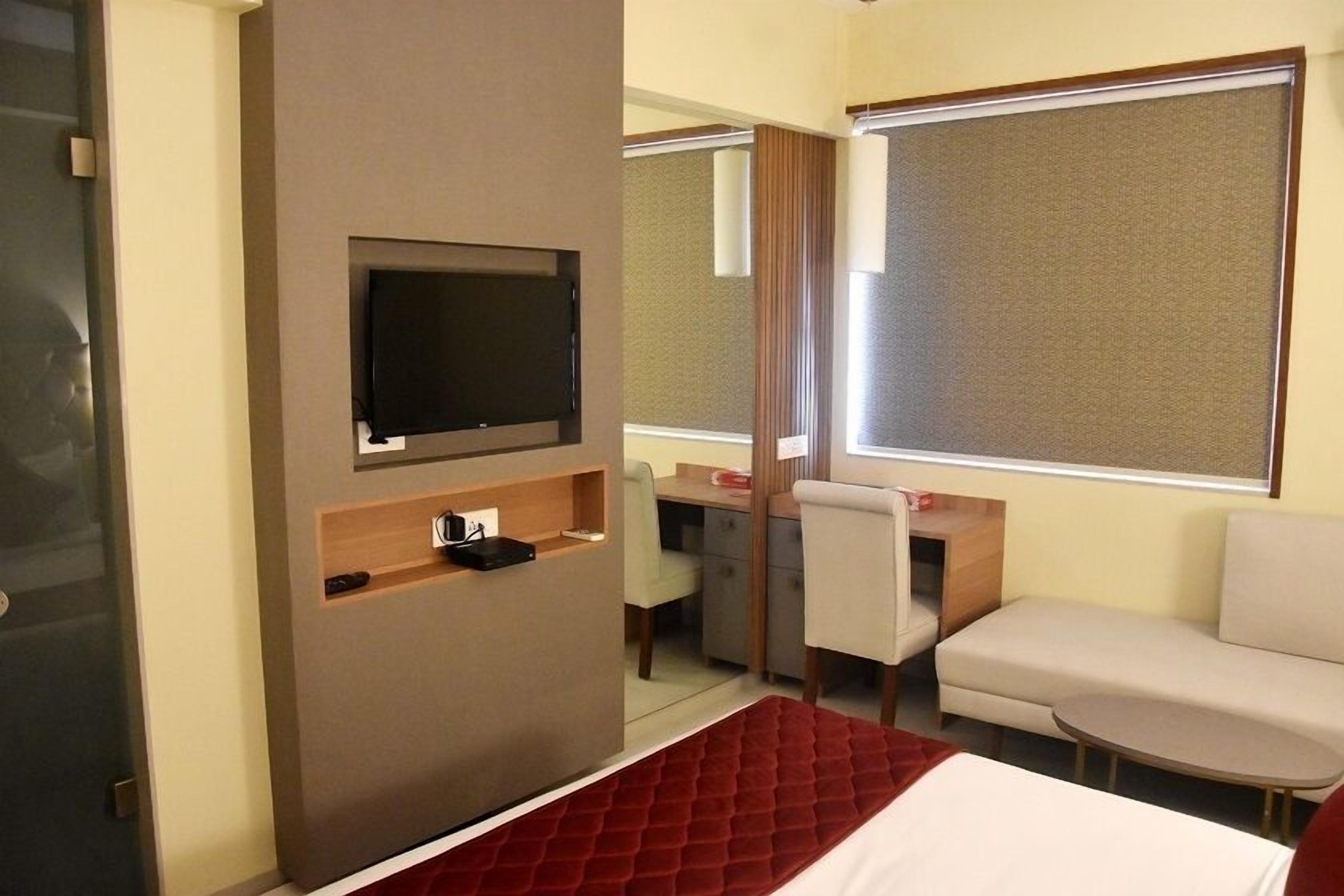A hotel room with a bed, a TV mounted on a wall, a desk with a chair, and a sofa.