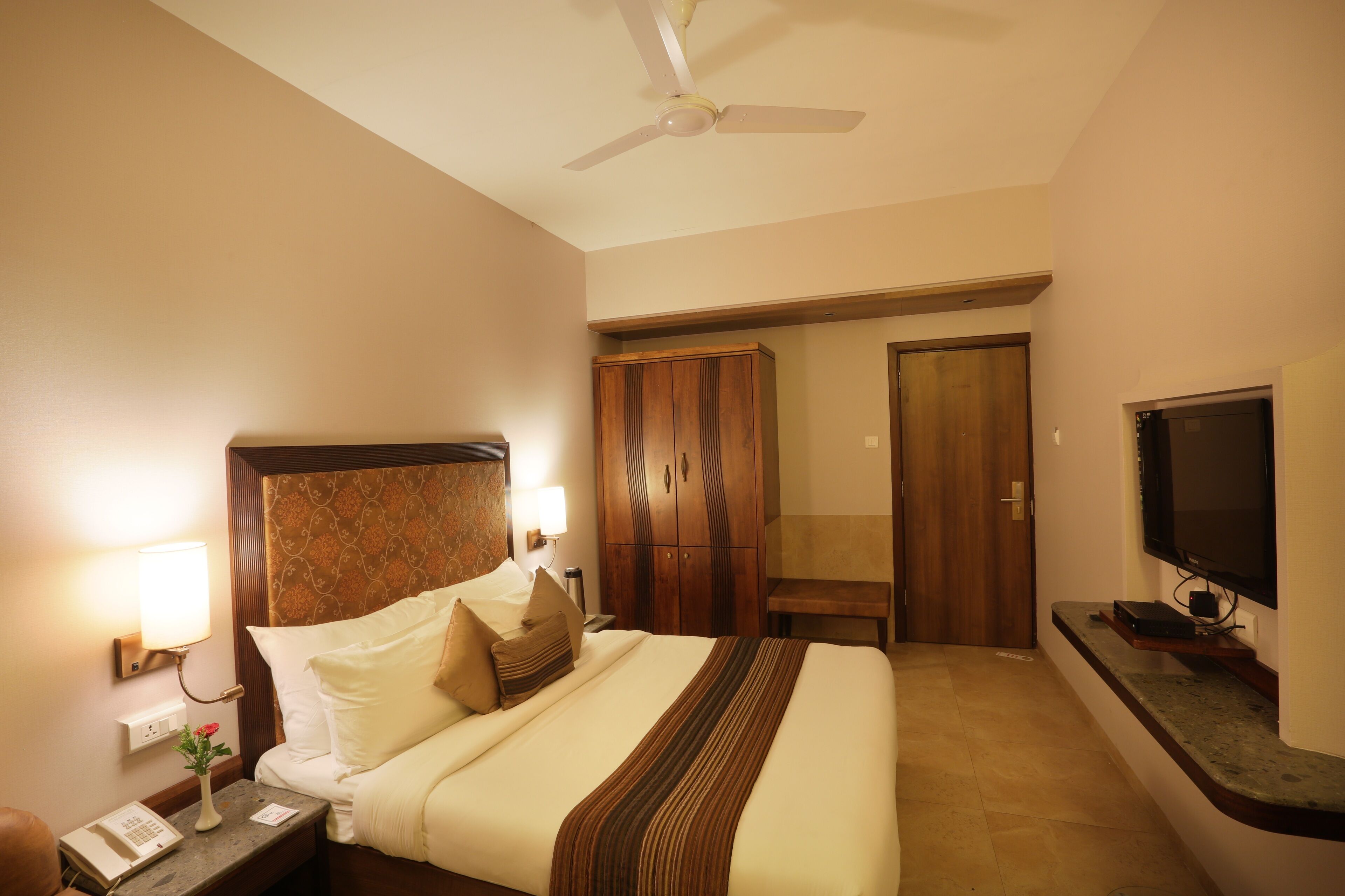 Une chambre d’hôtel comprenant un lit, une table de chevet, une lampe, une armoire et un téléviseur.
