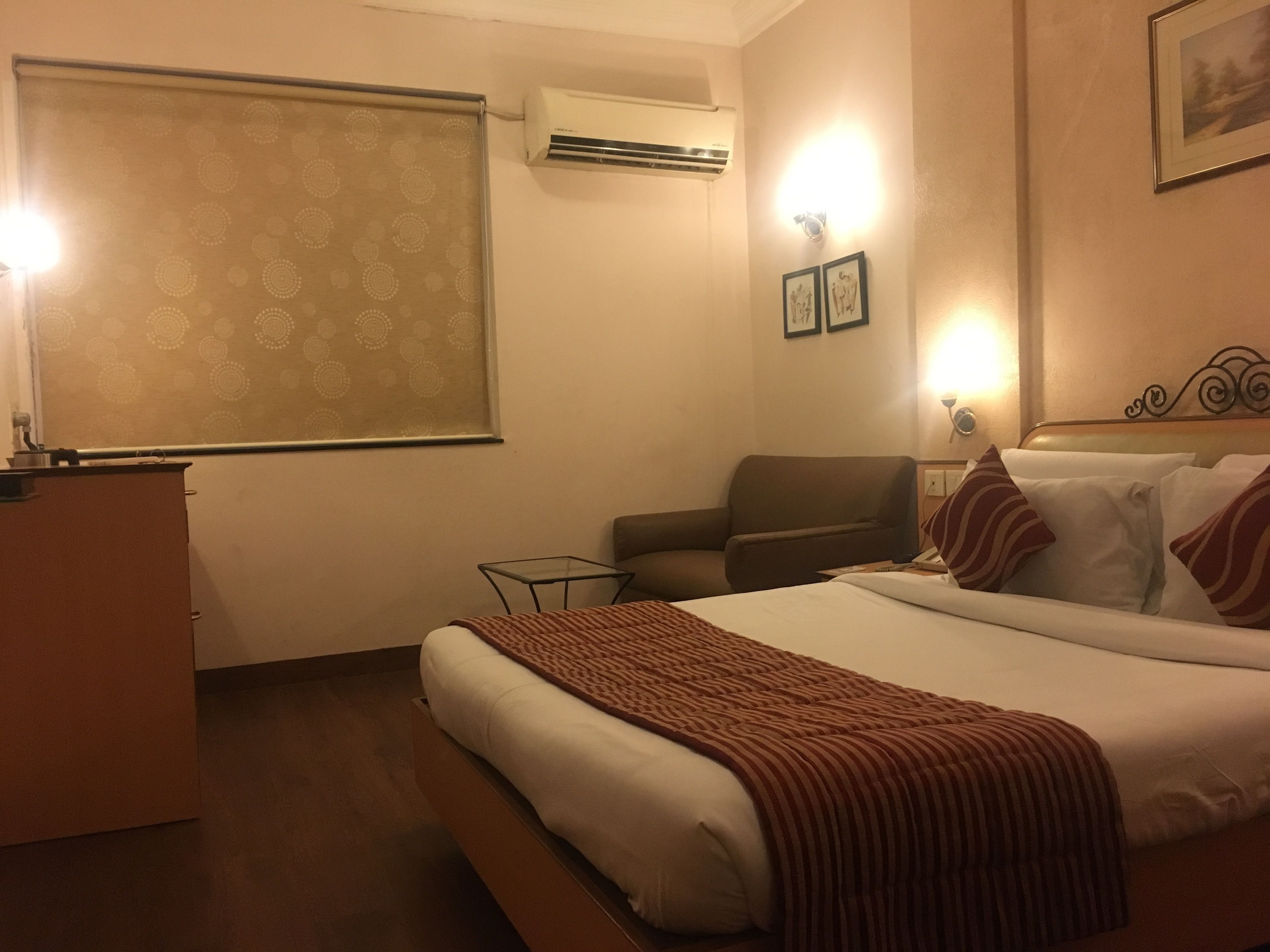 Een hotelkamer met een bed, een bureau, een stoel, een bijzettafeltje en een airconditioning.